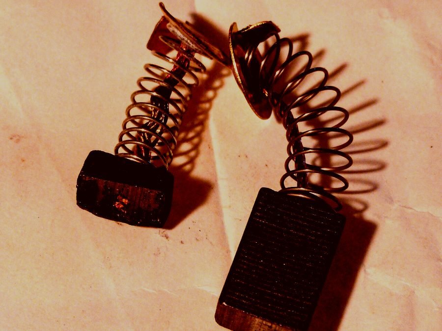 A worn carbon brush beside a new one, both with their copper springs