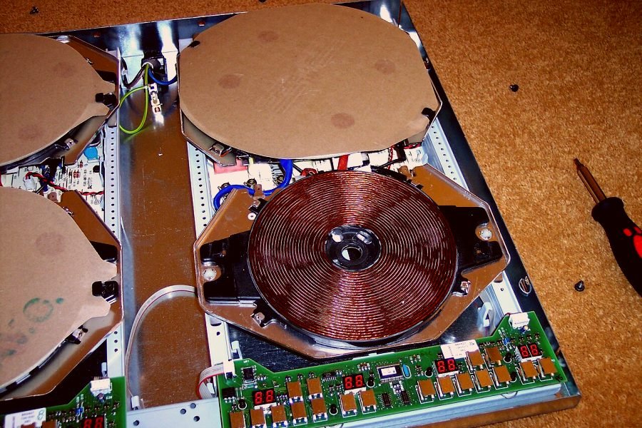 An induction cooktop opened on the bench with its coil and control board exposed