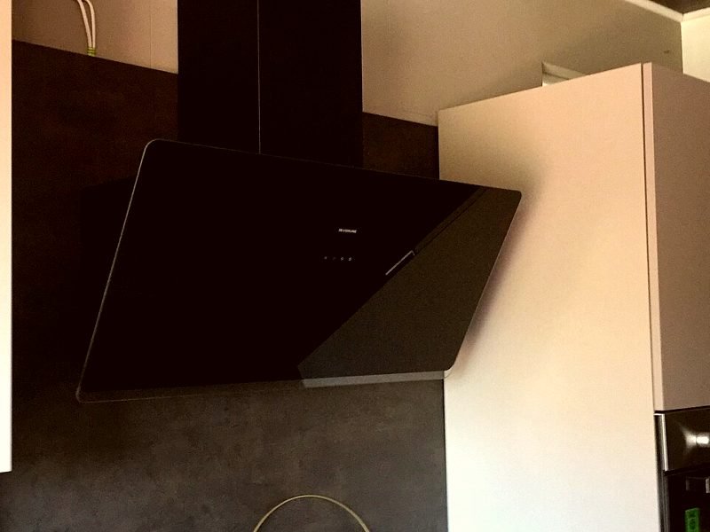 A black angled kitchen chimney mounted over a hob